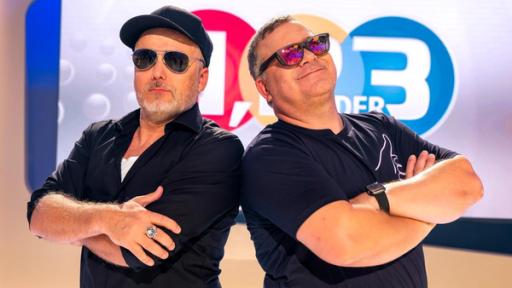 Sprache ohne Worte | Rechte: Ralf Wilschewski 1, 2 oder 3: Moderator Elton und Studiogast stehen vor der Vidiwall im "1, 2 oder 3"-Studio mit verschränkten Armen und Sonnenbrillen.
