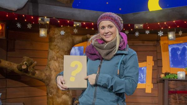 Singa steht im Baumhaus und hält einen Karton mit einem großen gelben Fragezeichen in der Hand.