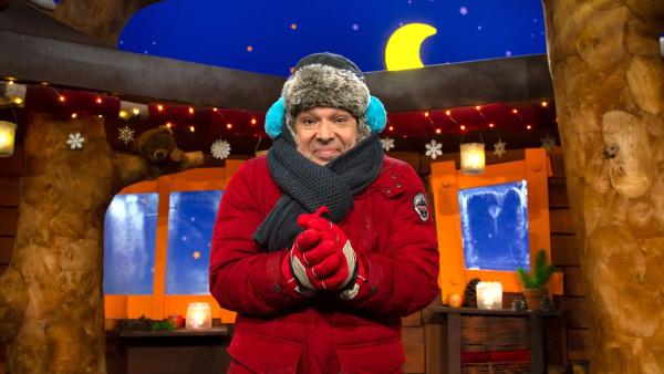 Juri steht im Baumhaus und trägt dicke Winterkleidung: Mütze, Ohrenwärmer, Schal und Handschuhe.