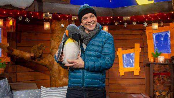 Juri steht im Baumhaus und hält ein Pinguin-Kuscheltier in der Hand.