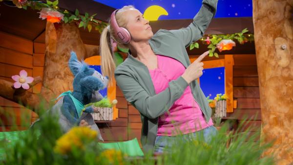 Singa trägt rosafarbende Kopfhörer und tanzt. Fidi sieht ihr dabei begeistert zu.