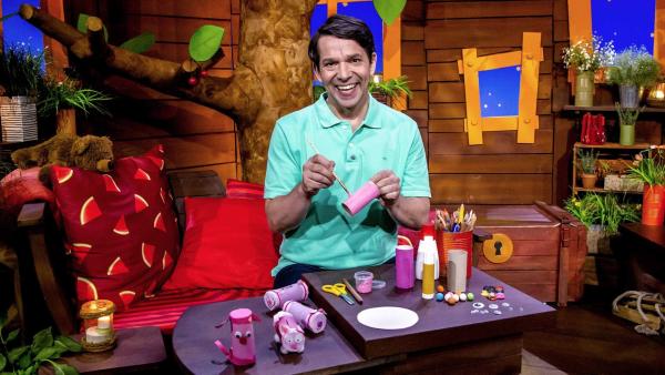 Juri malt eine Klopapierrolle mit einem Pinsel rosa an. Vor ihm stehen gebastelte Schweinchen.