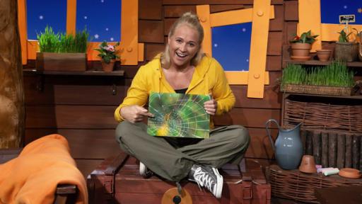 Rechte: KiKA Singa sitzt auf der Schatztruhe im Baumhaus. In der Hand jält sie ein Bild von einem Spinnennetz.