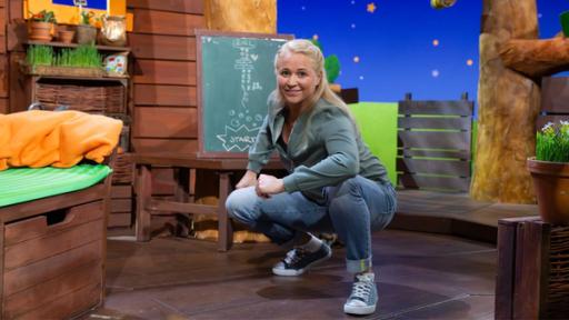 Rechte: KiKA Singa hockt im Baumhaus und lacht. Im Hintergrund sieht man eine Kreidetafel.