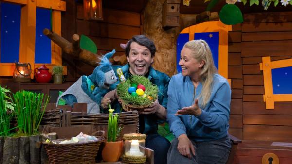 Fidi, Singa und Juri sitzen lachend im Baumhaus. Juri hält einen bunten Osterkorb.