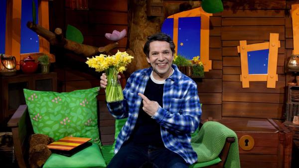 Juri sitzt im Baumhaus und hät eine Vase mit Narzissen in der Hand.