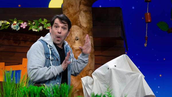 Juri schaut erschrocken. Neben ihm ist eine Figur unter einem weißen Laken.