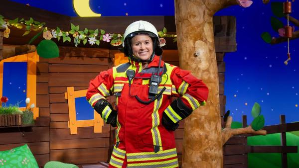 Singa steht selbstbewusst in kompletter Feuerwehrmontur im Baumhaus.