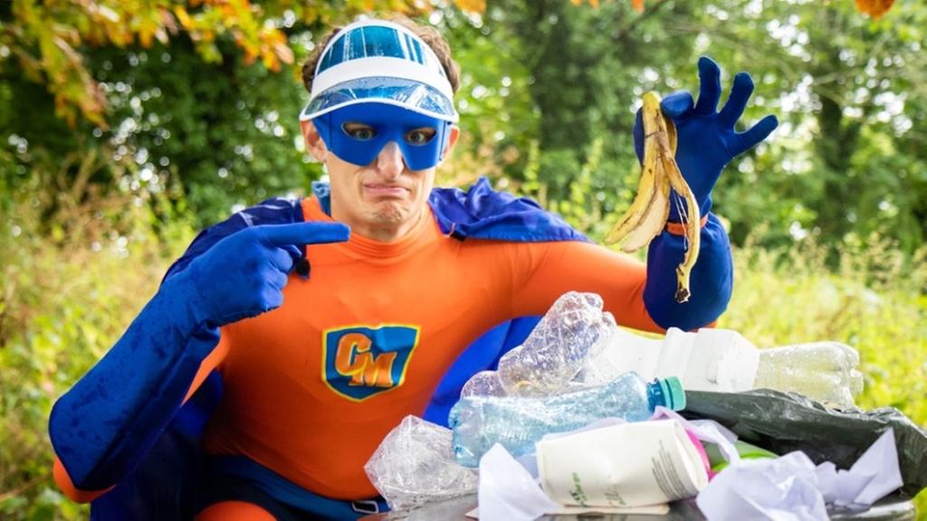 Werde zum Müll-Superheld | Julian im Superhelden-Kostüm vor einem vollgepackten Mülleimer. | Bild: BR/megaherz gmbh