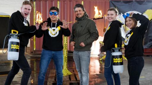 Bremsversagen, Spiegelgefängnis & Sturzregen | Rechte: ZDF in der Checkpoint-Halle v. l. n. r. Cem schaut mit dem Rücken zur Kamera in einen Spiegel, Tommy hält den rechten Daumen nach oben. Lisa und Trang stehen rechts neben ihm. Vorne auf dem Boden sitzend Mark mit einer Drohne in der Hand. Im Hintergrund ist das Checkpoint-Logo zu sehen.