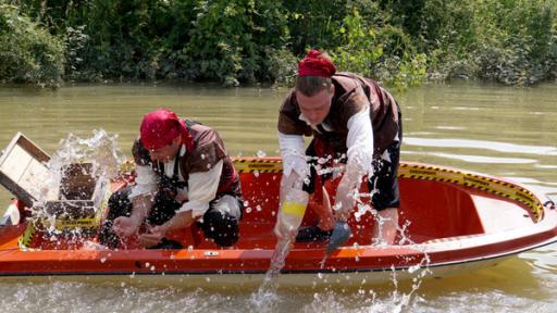 Zwei Jugendliche mit Piratenkopftuch schöpfen Wasser aus einem Boot.