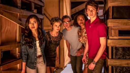 Kyra (Kimie Tsukakoshi), Imogen (Elizabeth Cullen), Peter (Jamie Carter), Ruksy (Rainbow Wedell) und Darra (Julian Cullen) stehen dicht nebeneinander in einem dunklen Raum zwischen Holzregalen. Sie schauen vorsichtig und aufmerksam in eine Richtung.