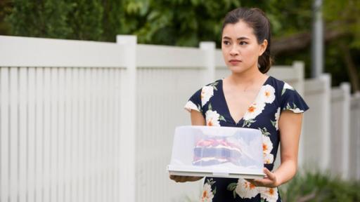 Kyra steht mit einem Kuchen in der Hand neben einem weißen Zaun.