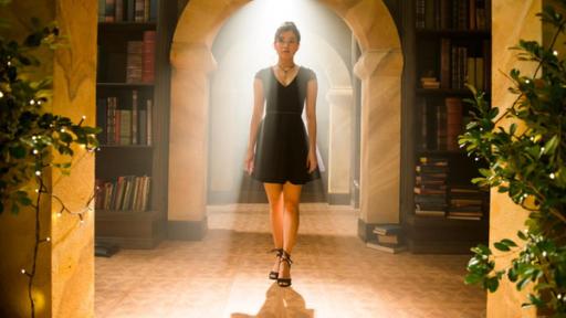 Kyra läuft in einem schwarzen Kleid durch die Bibliothek. Die Sonne scheint herein.