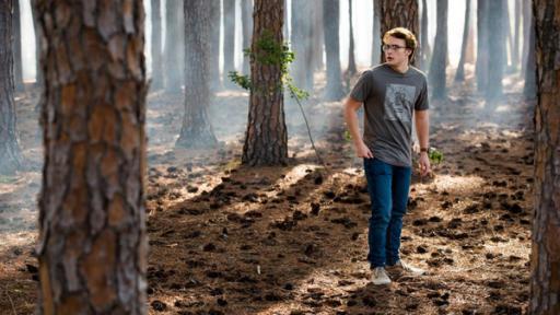 Peter steht inmitten von kahlen Bäumen im Wald.