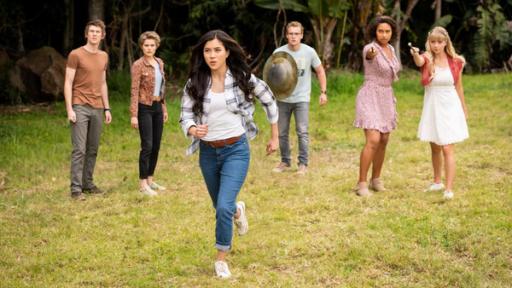 "Club der magischen Dinge - Keine Geheimnisse mehr":  Darra (Julian Cullen), Imogen (Elizabeth Cullen), Peter (Jamie Cullen), Ruksy (Rainbow Wedell) und Lily (Mia Milnes) stehen hinter Kyra (Kimie Tsukakoshi) auf einer Wiese, die von dichtem Wald umgeben ist. Kyra beginnt, auf ein vor ihr liegendes Ziel loszurennen. Ruksy und Lily strecken ihre Zauberstäbe nach vorne, Peter hält ein Metallschild in der rechten Hand vor dem Körper. Alle sind angespannt und schauen ernst nach vorne.