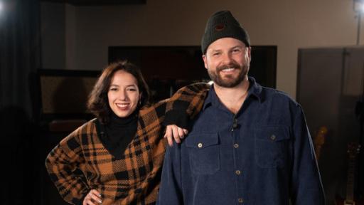 "Dein Song"-Kandidatin Estrela (18) und Musikpate Ian Hooper stehen nebeneinander in einem Tonstudio und lächeln freundlich in die Kamera. Dabei legt Estrela ihren Arm lässig auf Ians Schulter ab.