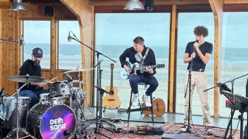Die Band spielt vor einem Panoramafenster zum Strand