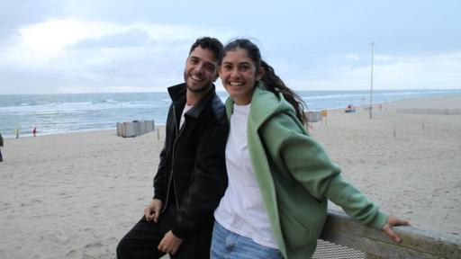 Eine junge Frau und ein junger Mann stehen lachend an einem Strand