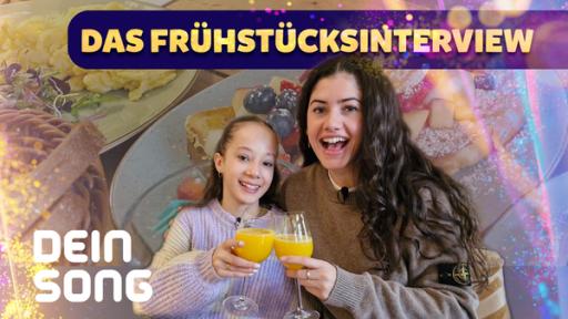 Jeannie und Mina lachen in die Kamera und stoßen mit einen Glas Orangensaft an.