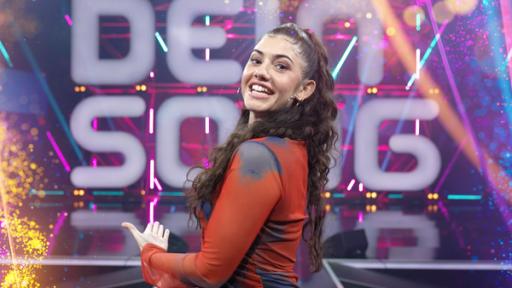"Dein Song"-Moderatorin Jeannie zeigt auf das "Dein Song"-Logo hinter sich auf der Bühne