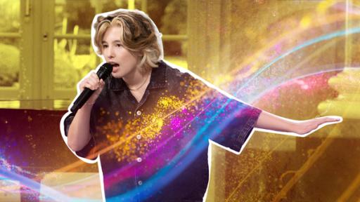 Paula singt. Ihr linker Arm ist ausgestreckt. Der Hintergrund ist golden.