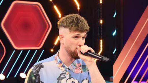 Rechte: KiKA/Steffen Becker “Beatboxer“ Madox perfomt im Studio vor einem Hintergrund mit grafischen Formen. Dabei hält er sein Mikrofon ganz nah am Mund.