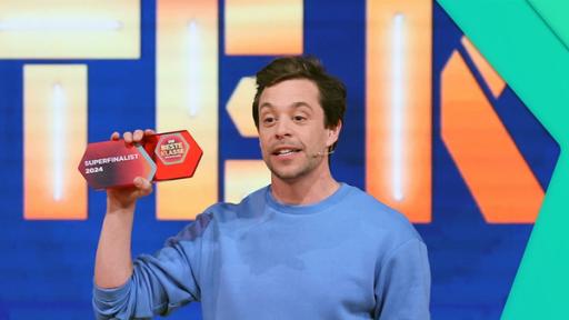 Rechte: KiKA/Steffen Becker Mittig steht Tobi. Er hält in seiner Hand ein kleines Schild aus Plastik mit der Aufschrift Superfinalist 2024 und dem Logo von Die beste Klasse Deutschlands. Im Hintergrund große Buchstaben.