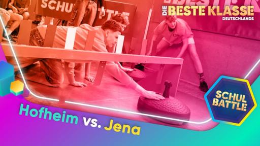 In einer Turnhalle zwei Schüler auf den Knien am Boden. Mit ausgestrecktem Arm berühren sie einen sehr großen Curling-Kegel, um ihn zu bewegen. Dahinter weitere Kinder, die zuschauen.