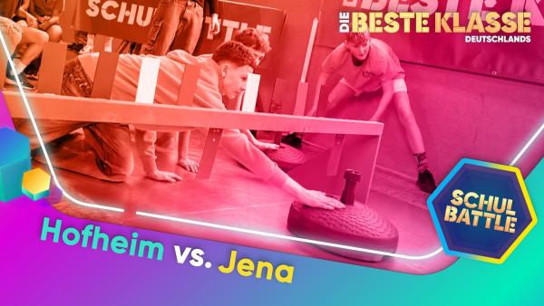 In einer Turnhalle zwei Schüler auf den Knien am Boden. Mit ausgestrecktem Arm berühren sie einen sehr großen Curling-Kegel, um ihn zu bewegen. Dahinter weitere Kinder, die zuschauen.