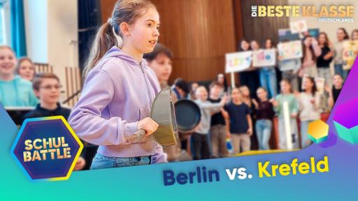 Rechte: KiKA/Bavaria Entertainment Ein Mädchen hält eine Pfanne abwehrend vor sich und schaut konzentriert. Im Hintergrund viele Kinder, die gespannt das Geschehen verfolgen und anfeuern. Einige halten Schrifttafeln. Unten der Text Berlin versus Krefeld und das Schulbattle-Logo.