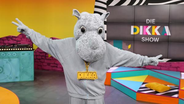 DIKKA, das rappende Nashorn steht mit ausgestreckten Armen im Studio der DIKKA-Show.