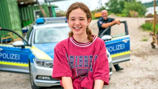 Leo steht lachend vor einem Polizeiwagen.