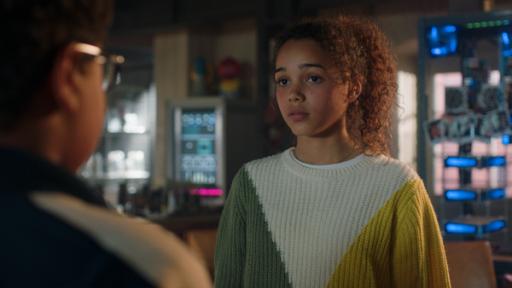 Taara trägt einen farbigen Pullover und ihre Haare sind zu einem Zopf gebundne. Im Hintergrund befindet sich die Pfefferkörner-Zentrale.