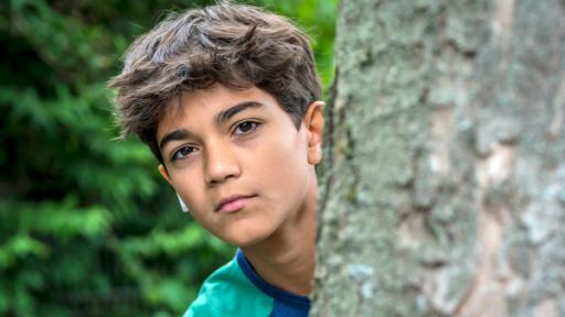 Hakim schaut hinter einem Baum hervor.