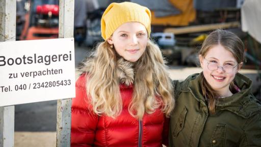 Stella (Zoë Malia Moon) und Pinja (Sina Michel) stehen neben einem Schild der Bootslagerei.