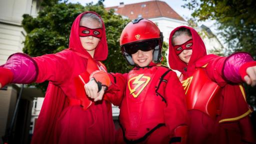 Die Superhelden | Rechte: NDR/Studio HH Foto: Boris Laewen Stella (Zoë Malia Moon, links), der Rote Blitz (Lilly Barshy, Mitte) und Pinja (Sina Michel) in roten Superhelden-Kostümen.