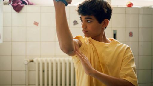 Muskeln um jeden Preis | Rechte: NDR/Letterbox Hakim (Mads Albatross) schaut seine Oberarmmuskeln im Spiegel an und ist unzufrieden.