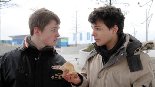 Ein Jugendlicher  (Lukas Kieback, rechts) hält einem anderen (Maximilian Werner) einen Geldschein hin. Sie sehen sich an.