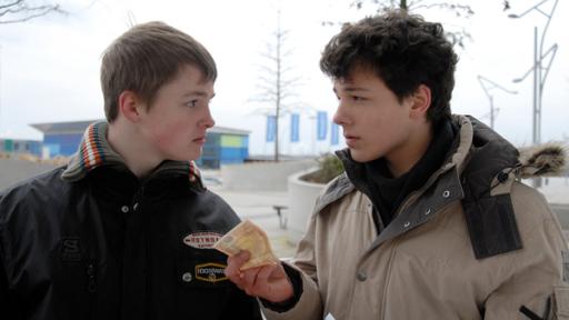 Ein Jugendlicher  (Lukas Kieback, rechts) hält einem anderen (Maximilian Werner) einen Geldschein hin. Sie sehen sich an.