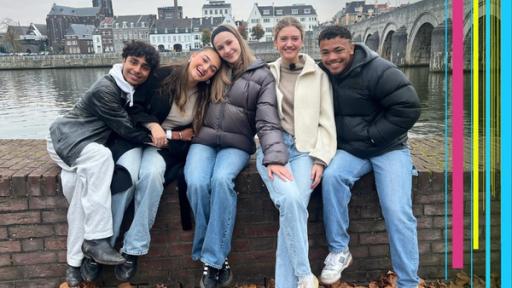Malik, Sofia, Toni, Emma und Chinedu sitzen auf einer Mauer - im Hintergrund die Stadt