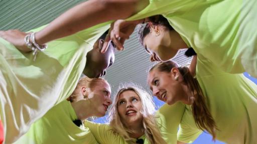 MWG Porto - Gewinner oder Verlierer? | Rechte: ZDF, E+U TV Fünf Mädchen in neongelben T-Shirts stecken als Team im Kreis die Köpfe zusammen und haben sich die Arme gegenseitig über die Schultern gelegt. Der Fotograf steht unterhalb von Ihnen und blickt nach oben in die eifrigen Gesichter. Die fünf Mädchen besprechen offenbar eine Spiel-Taktik. Die Mädchen wirken etwas zerzaust, aber fröhlich.