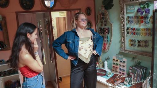 MWG Porto - Shoppingtour durch Porto | Rechte: ZDF, E+U TV Zwei Mädchen stehen in einem Laden und probieren offenbar Kleidung und bunte Sonnenbrillen aus. Ein blondes Mädchen hat die Hände in die Hüften gestemmt und betrachtet sich offenbar in einem Spiegel, der am Bildrand zu erahnen ist. Ein Mädchen mit dunkelbraunen, langen Haaren beobachtet sie und hält kritisch die Hand an die Lippen.