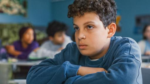 Echt Friends - Teaser - Folge 7 | Rechte: © ZDF / Studio Zentral Im Klassenraum sitzt Tom mit verschränkten Armen an seinem Tisch und schaut traurig nach vorne. Im Hintergrund sind noch andere Mitschüler verschwommen zu erkennen.