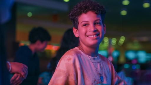 Echt Friends - Teaser - Folge 10 | Rechte: © ZDF / Studio Zentral Tom steht strahlend im Bowlingcenter, sein Gesicht ist in rötliches Licht getaucht. Im Hintergrund ist Pit zu erkennen und andere Kinder. Blaue, grüne und pinke Spots sind rechts zu sehen.