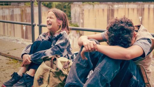 Echt friends - Teaser - Folge 5 | Rechte: © ZDF / Studio Zentral Am Rand eines stillgelegten Gasometers sitzen Liv und Pit am Geländer. Zwischen ihnen steht Pits Rucksack. Liv lacht lauthals, Pit hat seinen Kopf auf seine Knie gelegt, die er mit verschränkten Armen umfasst.