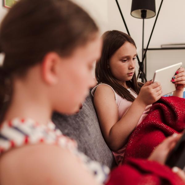 Zwei Mädchen sitzen auf einer Couch und halten Tablet und Smartphone in der Hand.