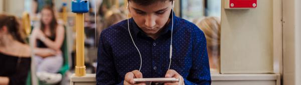 Ein Junge sitzt mit Smartphone und Kopfhörern in einem öffentlichen Verkehrsmittel.