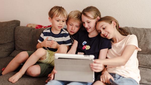 Zwei Jungen und zwei Mädchen sitzen auf einer Couch und schauen auf ein Tablet.