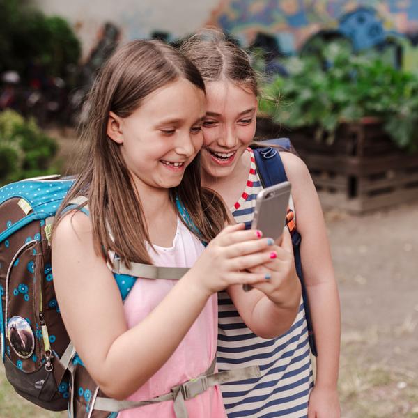 Zwei Mädchen stehen auf einem Schulhof uns schauen auf ein Smartphone.